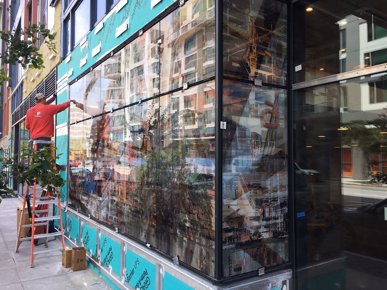 Worker on a ladder beside a ground-floor wall of large printed glass panels